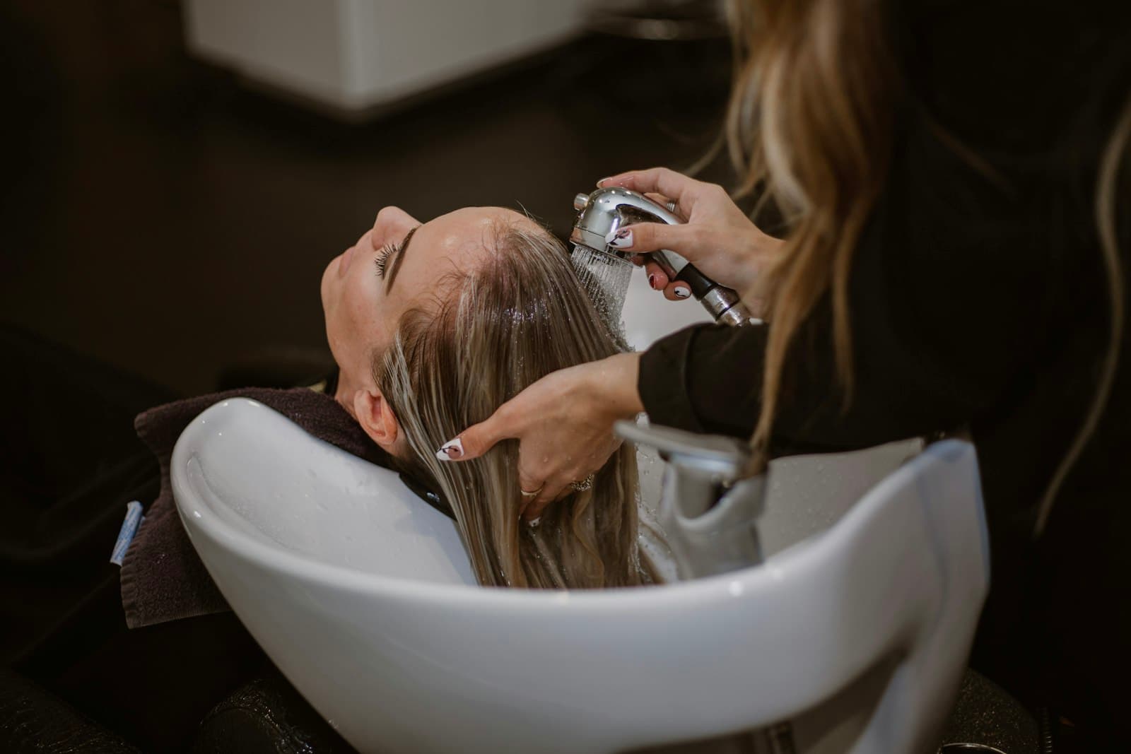 A stylist blow-drying a client's hair at a salon station