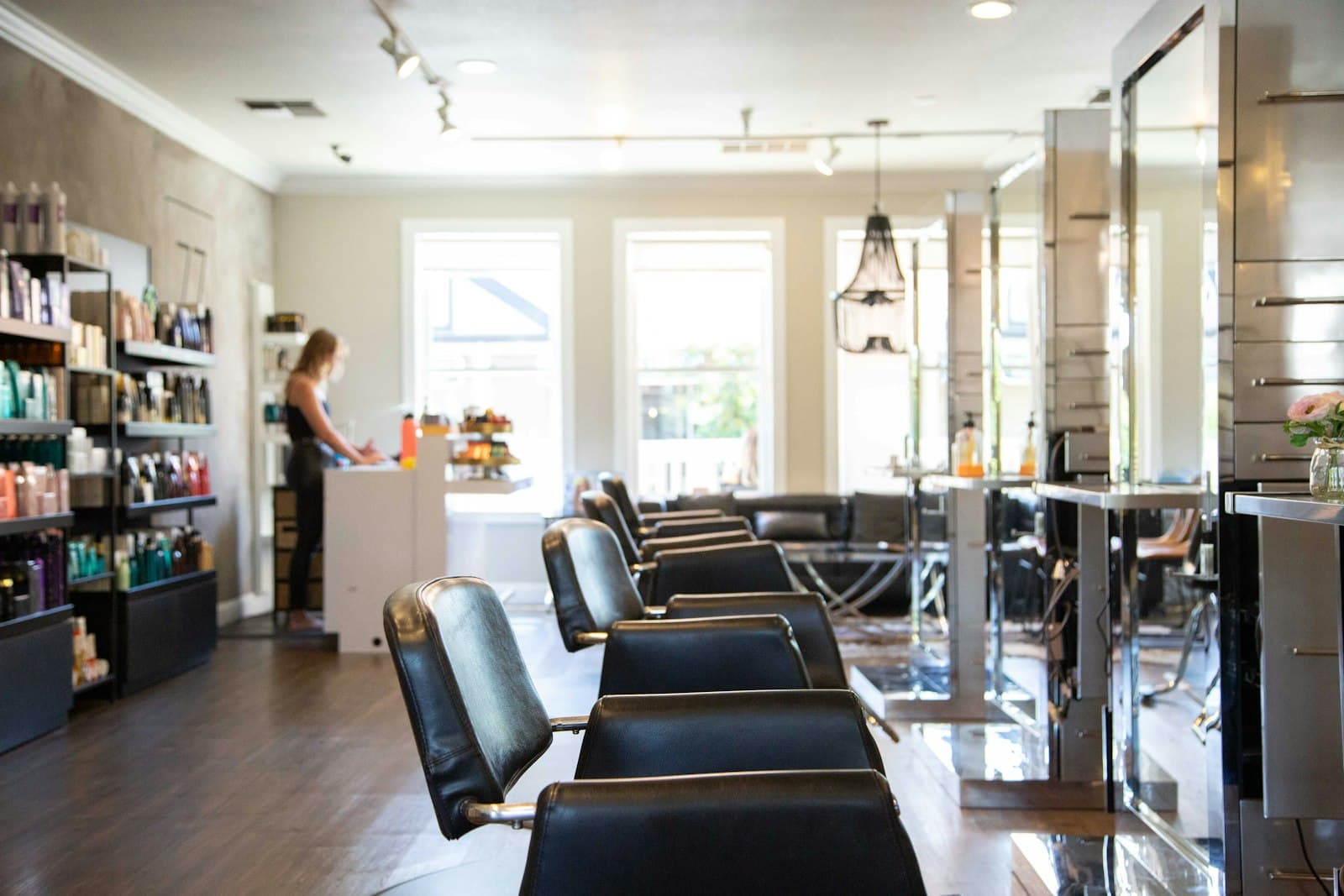 A bright salon floor with a row of black styling chairs and product shelves