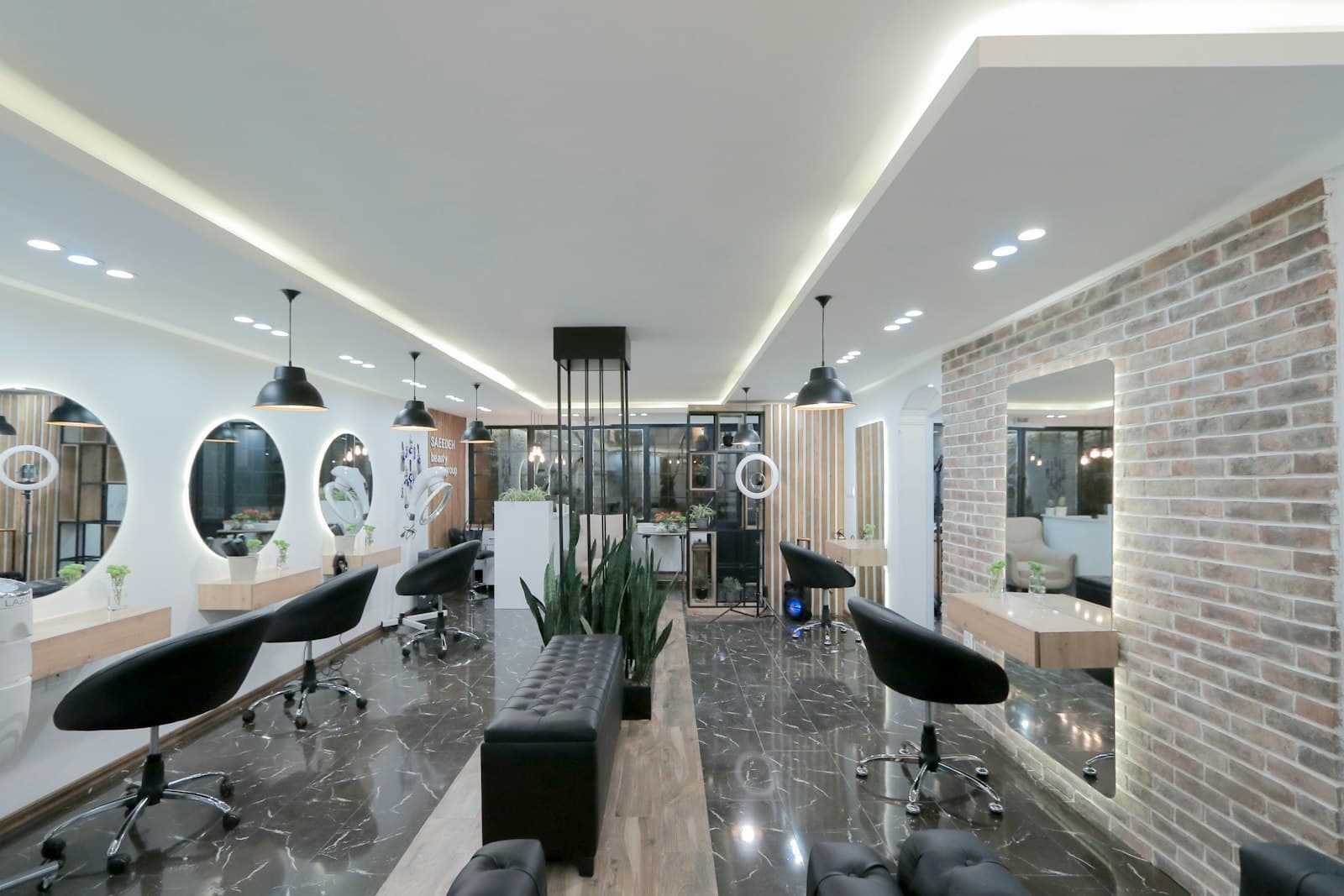 A modern salon with black styling chairs, round mirrors and a brick wall
